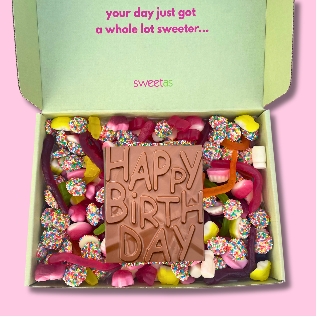 Box of assorted candies with a chocolate bar that says 'Happy Birthday' on a pink background, featuring the brand 'sweetas'.