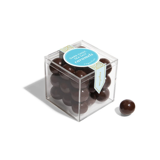 Clear cube box filled with chocolate-covered caramel on a white background