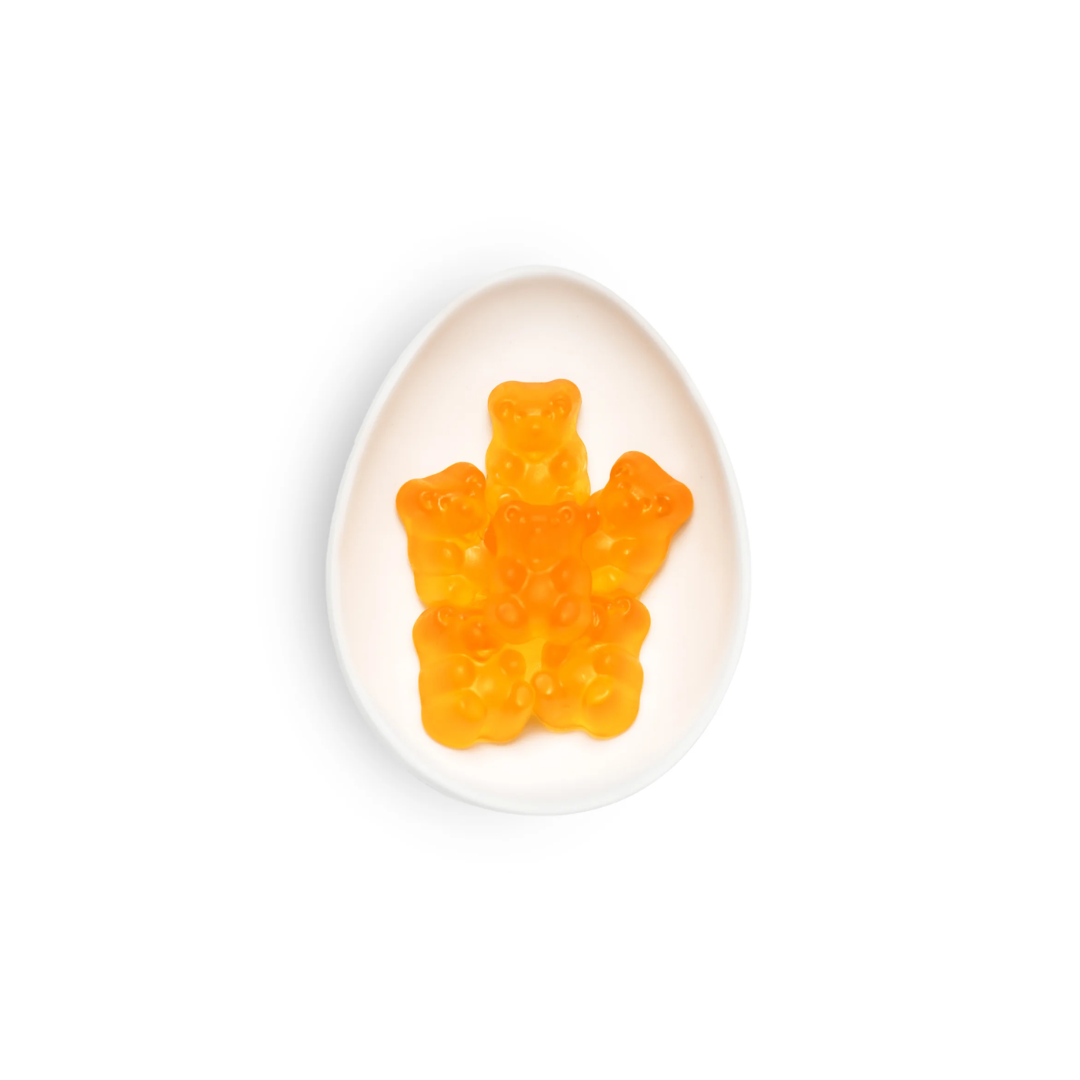 Orange gummy bear on a white egg-shaped container against a white background