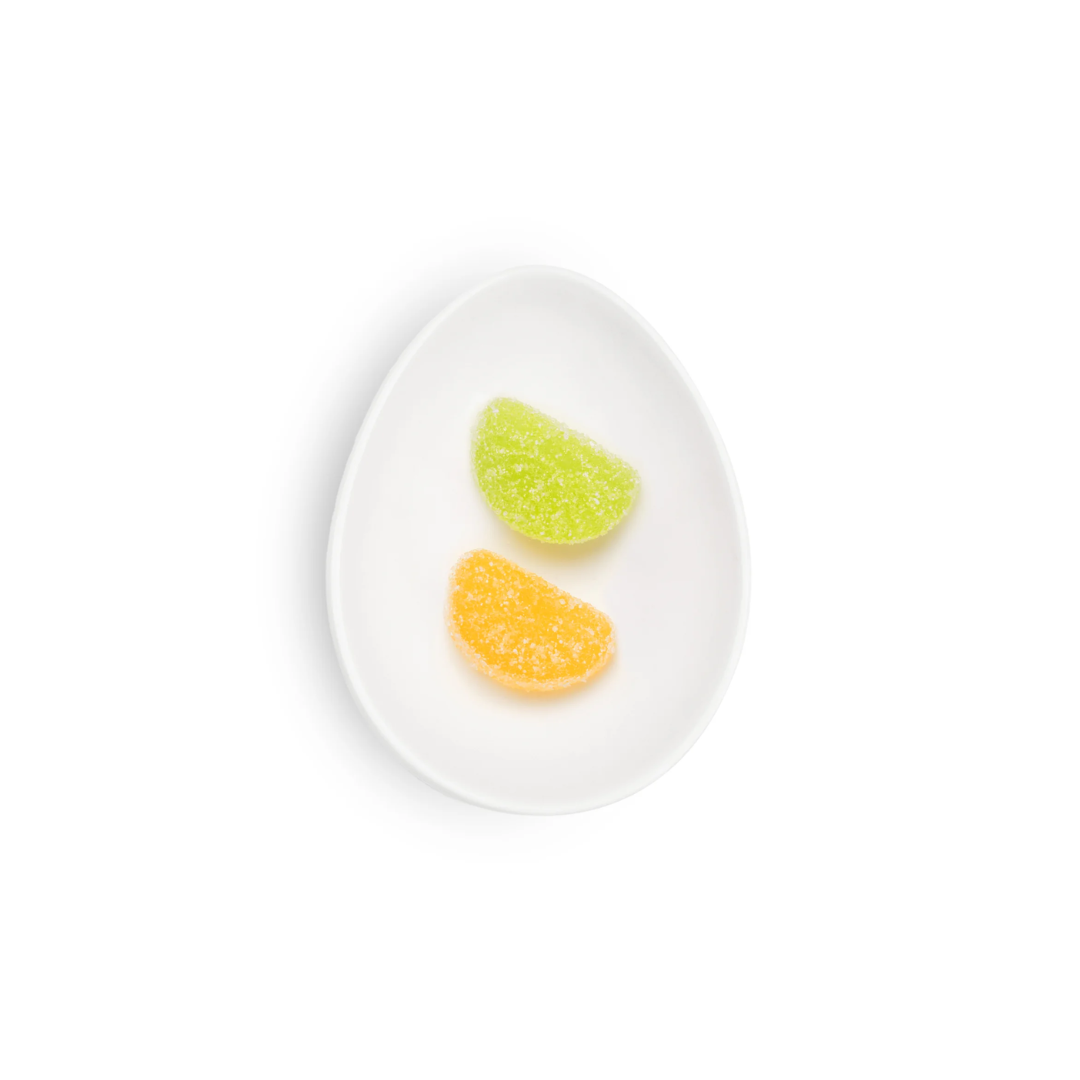 Two gummy candy slices, one green and one orange, on a white plate against a white background.